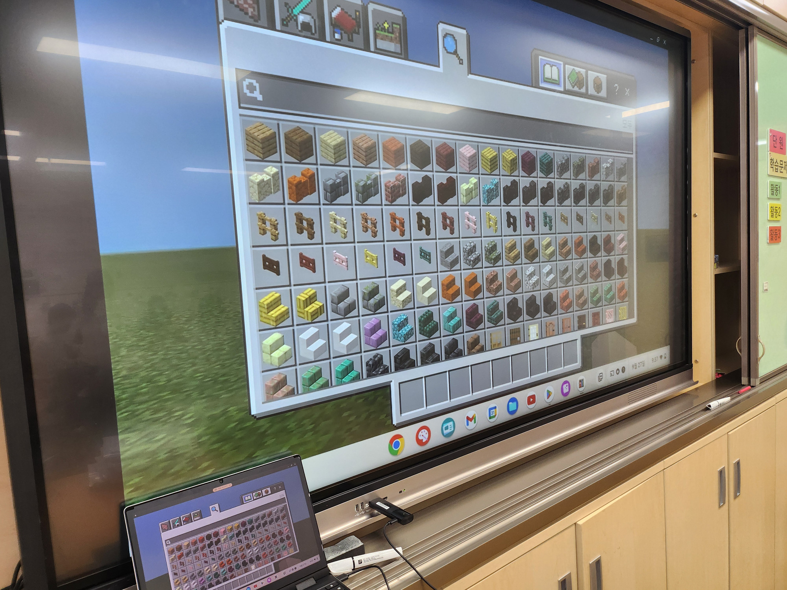 교실의 큰 화면과 교사용 기기에서 Minecraft 블록 재료를 함께 살피는 장면